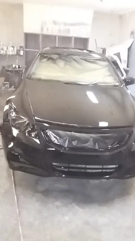 Black coupe with its windshield masked in plastic after front-end paint work
