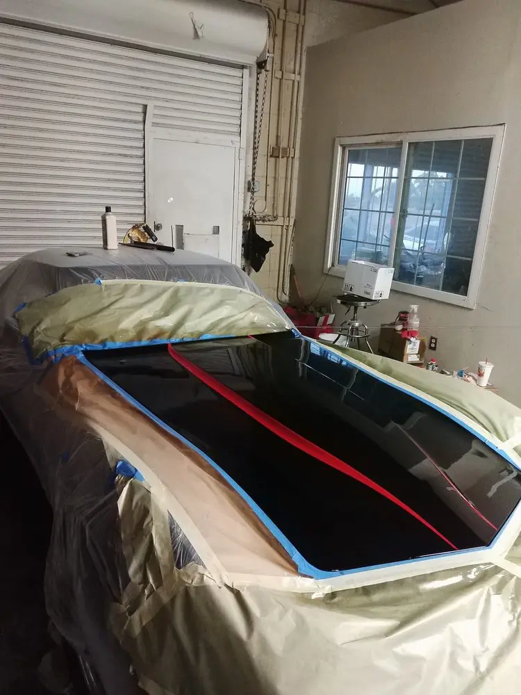 Black hood with fresh red stripes, the car masked in paper inside the shop
