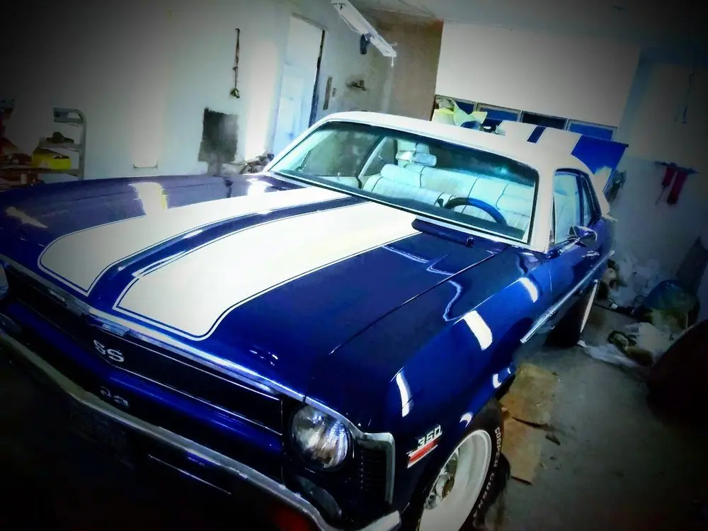 Blue Chevrolet Nova SS with fresh white racing stripes parked inside the body shop