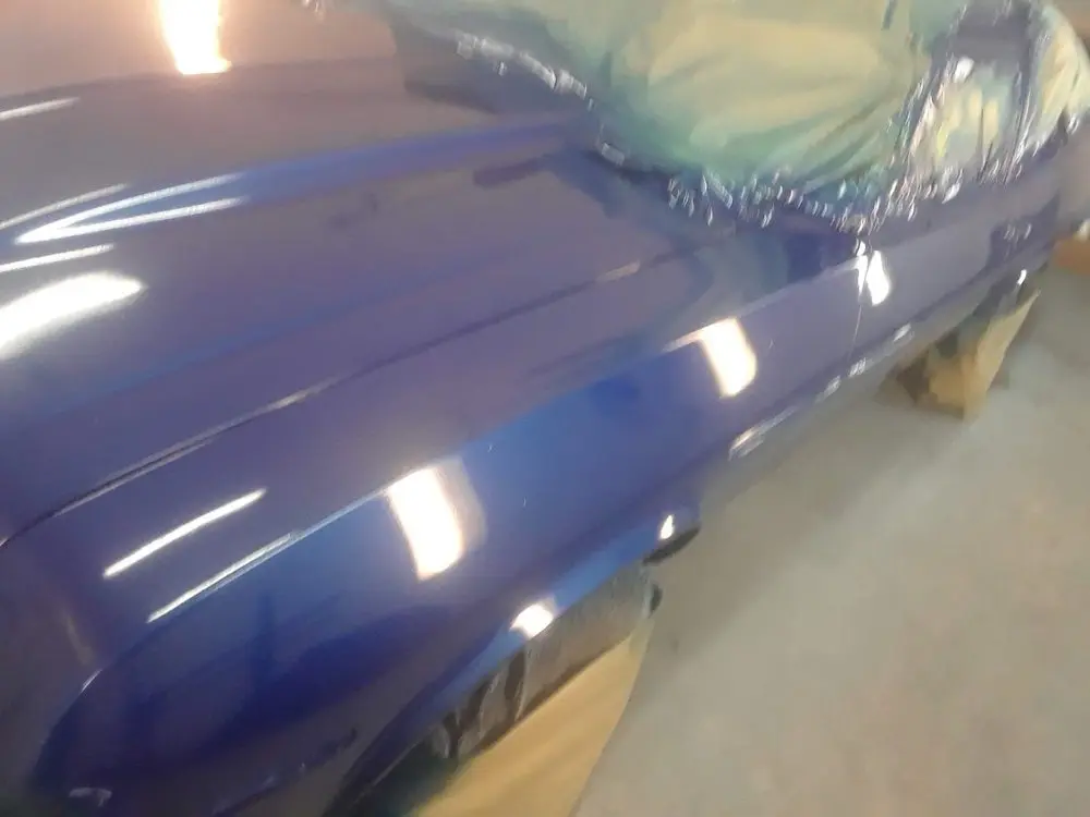 Close-up of fresh blue paint shining on a car's fender in the booth