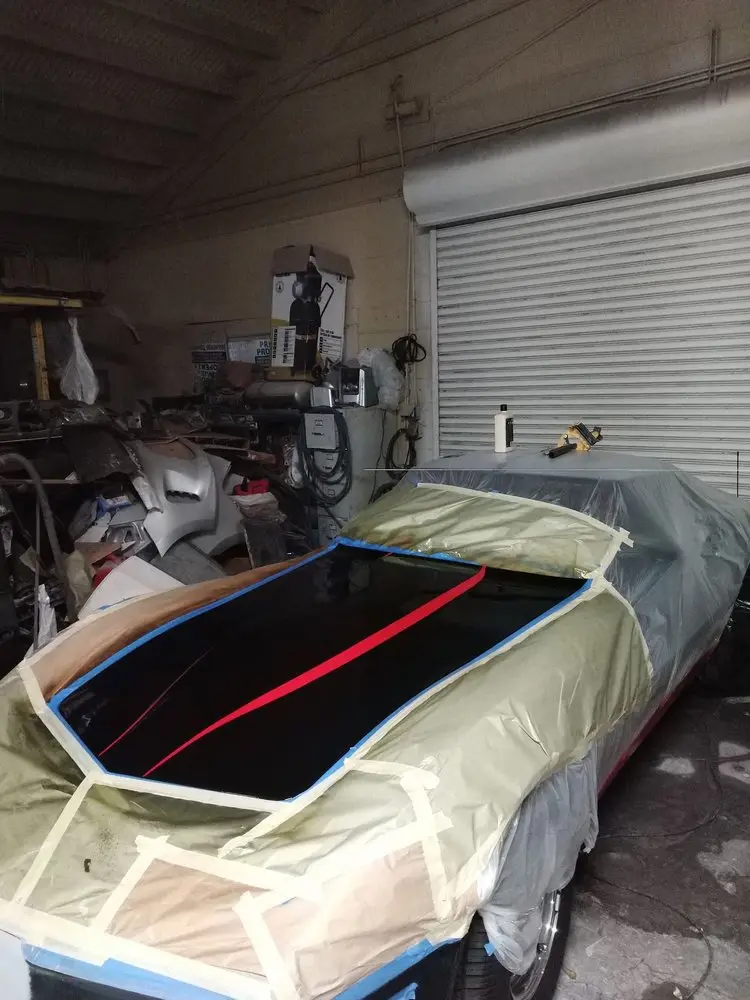 Classic car hood with red stripes painted, the body masked for paint in the shop
