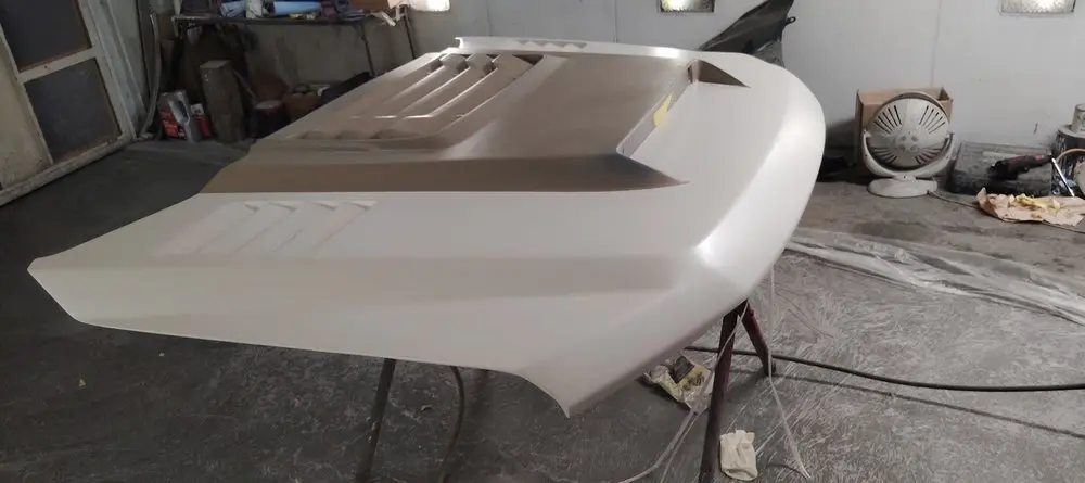 Fiberglass hood with vents, primed and resting on a stand in the shop