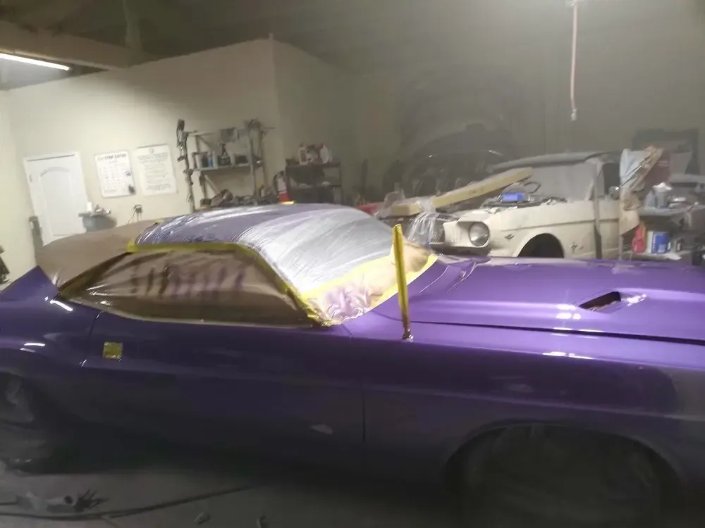 Purple car with its roof masked in plastic for paint inside the shop