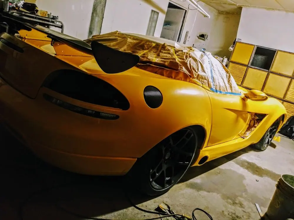 Rear quarter of a yellow sports car with fresh paint and masked spoiler