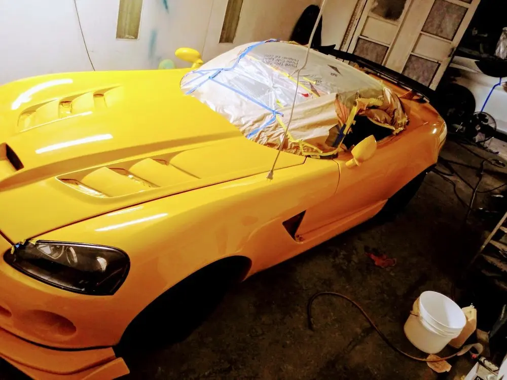 Freshly painted yellow sports car hood with windshield masked in the shop